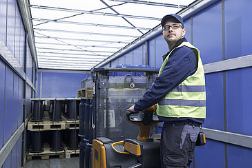 A Leadec employee with safety vest loading a coil pallet from a truck with an electric pallet truck.